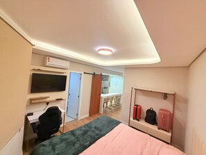 Ein Hotelzimmer mit Bett, Schreibtisch, Stuhl, Fernseher, Kleiderschrank und Gepäckablage.