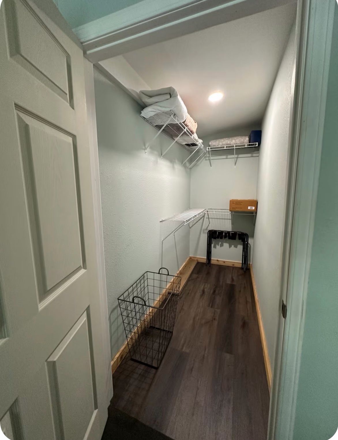 A narrow hallway with a wooden floor, a metal laundry rack, and a small storage bin.