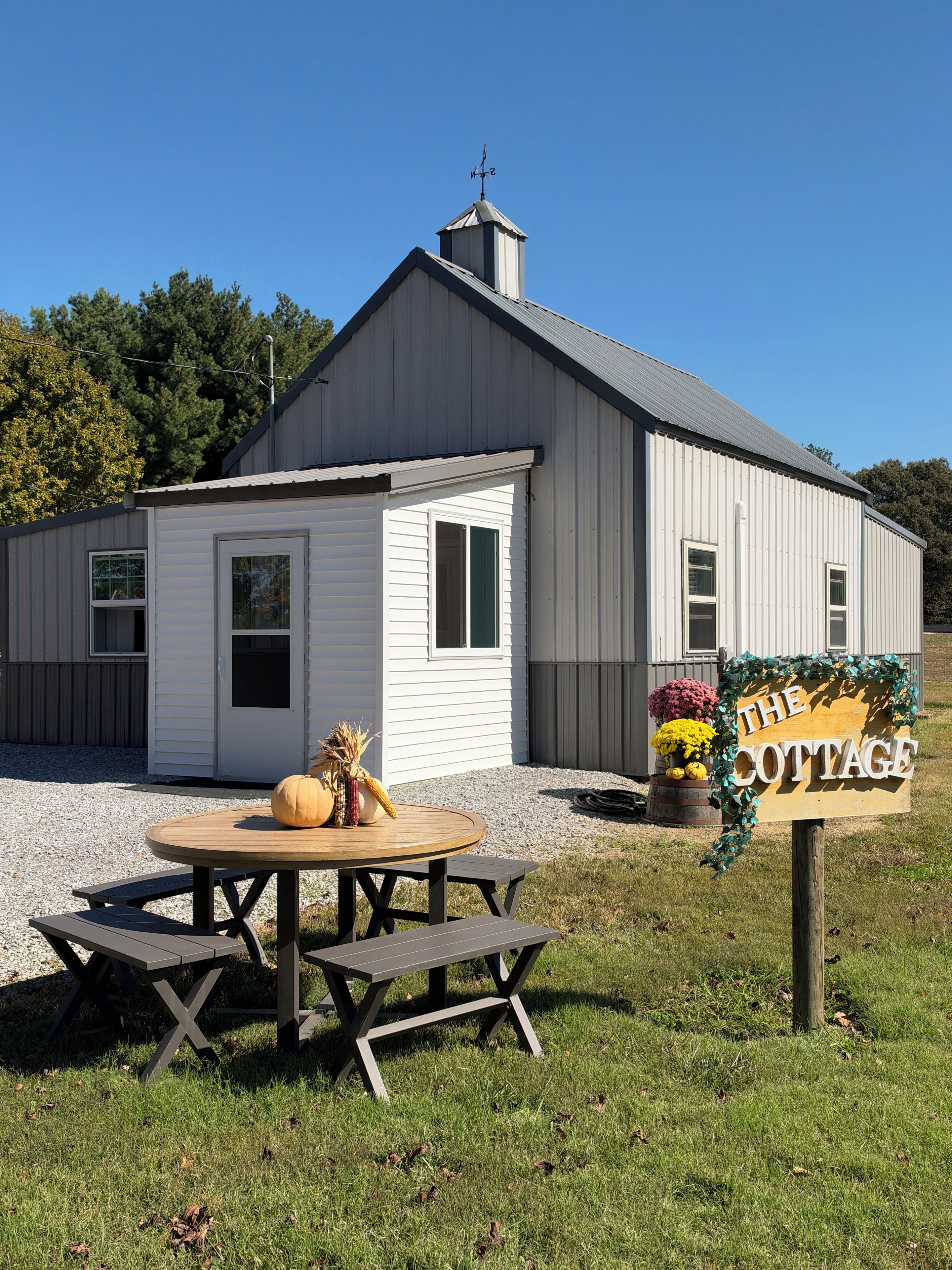 A rustic cottage with a metal roof, a wooden table with benches, and a sign that reads 'The Cottage'.