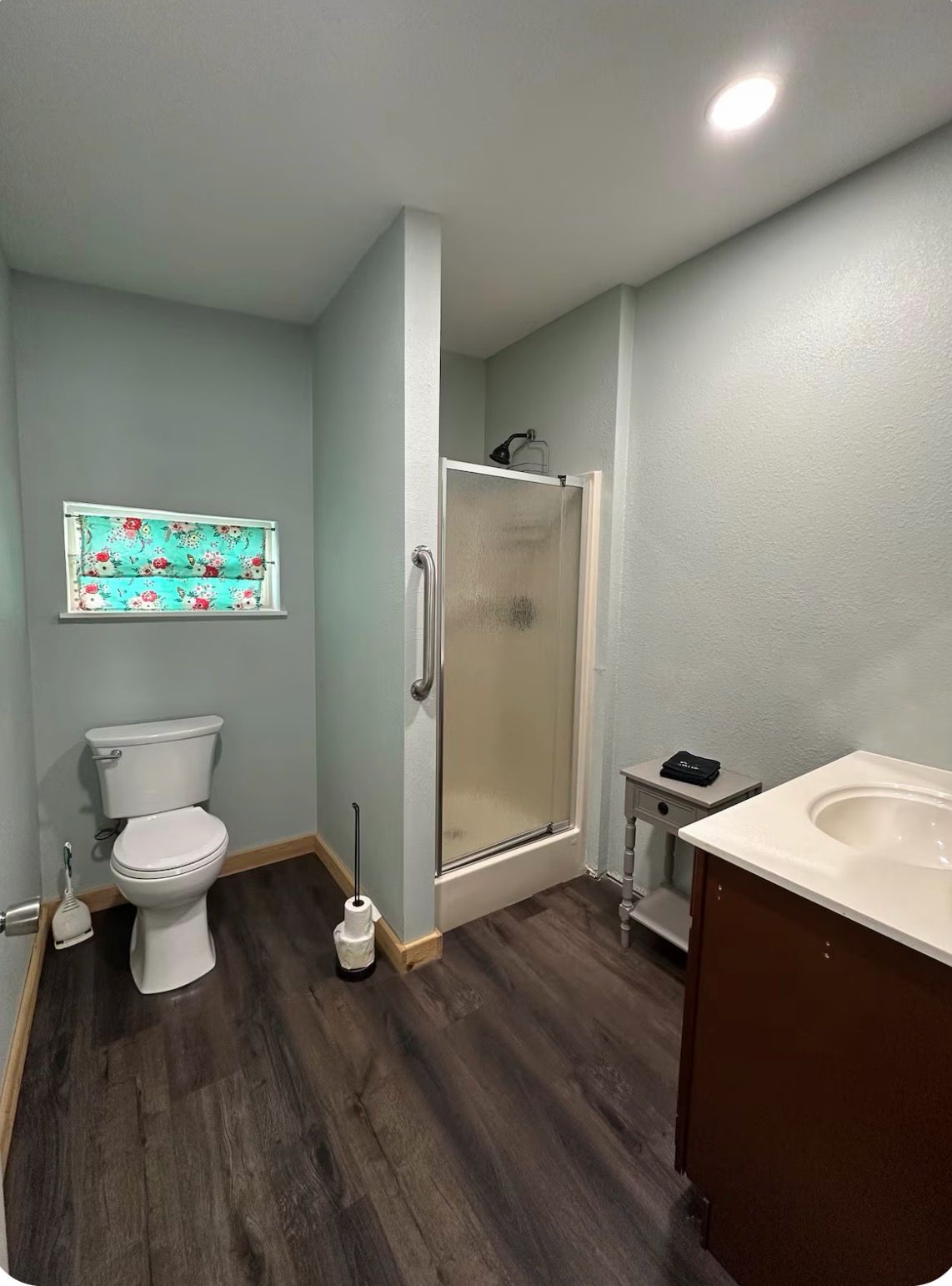 A bathroom with a toilet, a shower enclosure, a sink, and a window with a floral pattern.