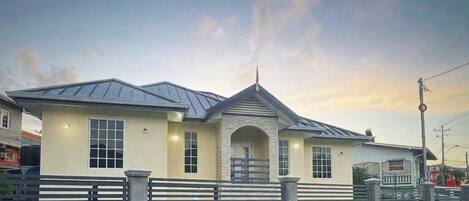 A two-story house with a stone facade, a metal roof, and a gated entrance.
