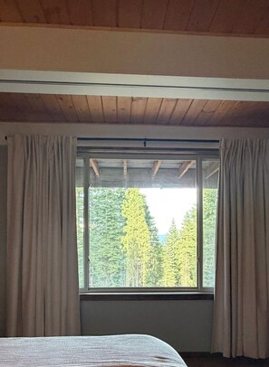 Ein Zimmer mit einem großen Fenster, Holzbalken an der Decke und einem Bett mit gestreifter Bettdecke.