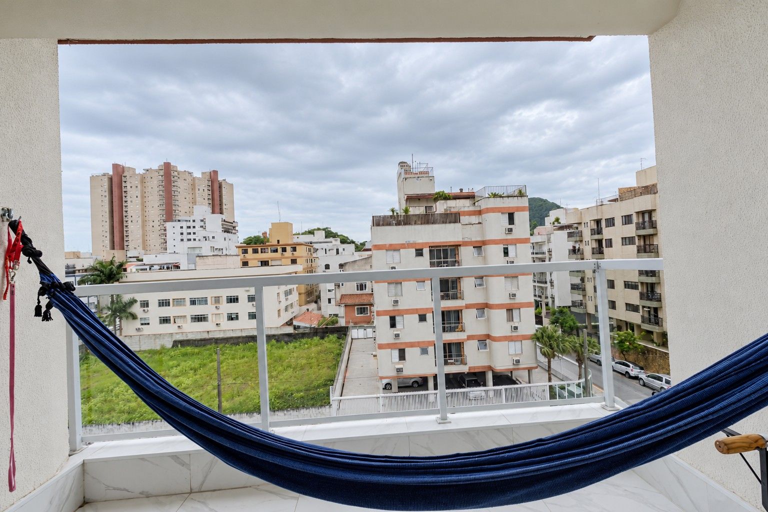 A balcony with a hammock, overlooking a residential area with multiple buildings and a clear sky.