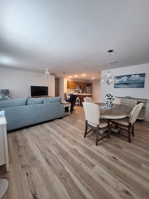 A modern living room with a sofa, TV, and dining area with a table and chairs. - Paradise in Spanish Springs 2/2/1.5 garage w/ 4-seat gas golf cart. Pet friendly (Lady Lake)