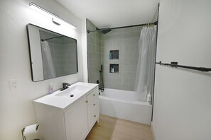 Een badkamer met een wit wastafelmeubel, spiegel en bad.