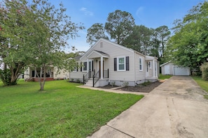 A single-story mobile home with a front porch, a small front yard, and a driveway leading to a garage. - Downtown Greer Furnished Southern Charmer (Greer)