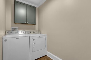 A laundry room with two Maytag washers and dryers, a cabinet above, and beige walls. - Downtown Greer Furnished Southern Charmer (Greer)