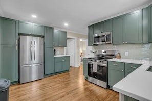A modern kitchen with stainless steel appliances, teal cabinetry, and a wooden floor. - Downtown Greer Furnished Southern Charmer (Greer)