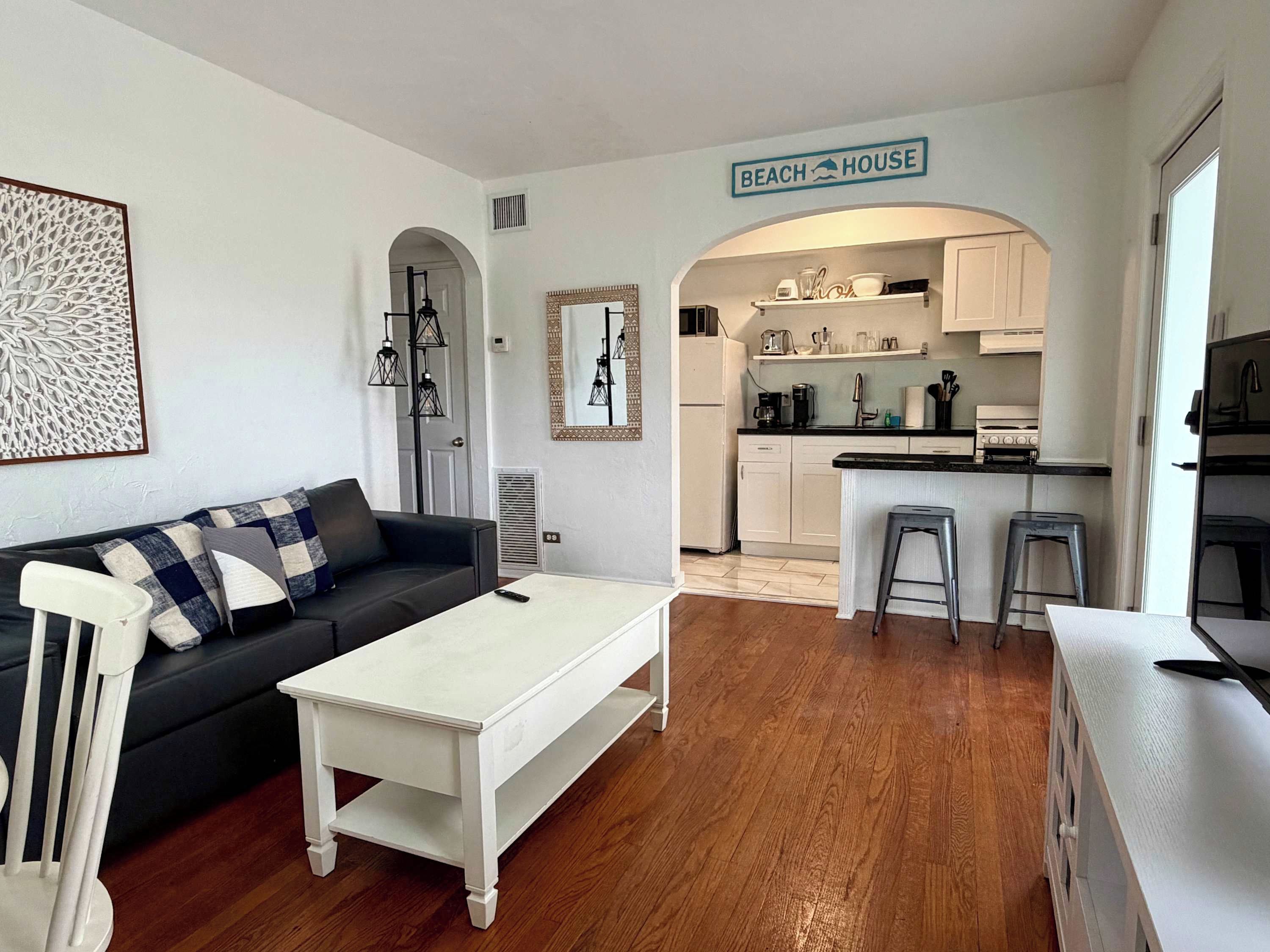 Um espaço de estar compacto com cozinha compacta, um sofá, uma mesa de centro e uma placa com a inscrição 'BEACH HOUSE'.