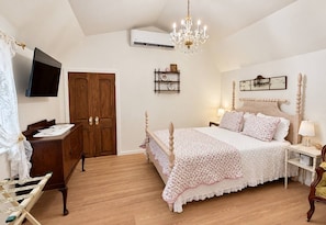 Ett sovrum med en säng i trä, ett skrivbord, en tv och en kristallkrona.