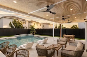 Un espace piscine extérieur avec des chaises longues, une table et des ventilateurs de plafond.