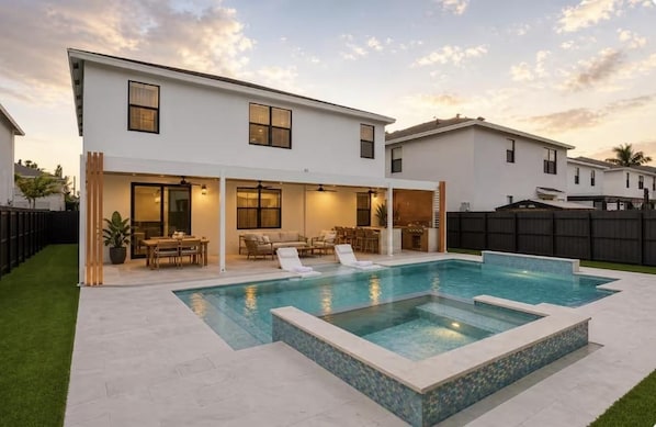 Une maison moderne à deux étages, dotée d’une piscine, de mobilier d’extérieur et d’une pelouse bien entretenue.