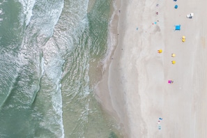 Vue aérienne d’une plage avec des personnes, des parasols et des chaises de plage.