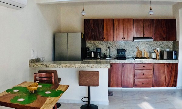 A compact kitchen with wooden cabinets, a refrigerator, a coffee maker, and a microwave. - 1 Bedroom Playa La Ropa Condo with a Pool and Views! (Zihuatanejo)