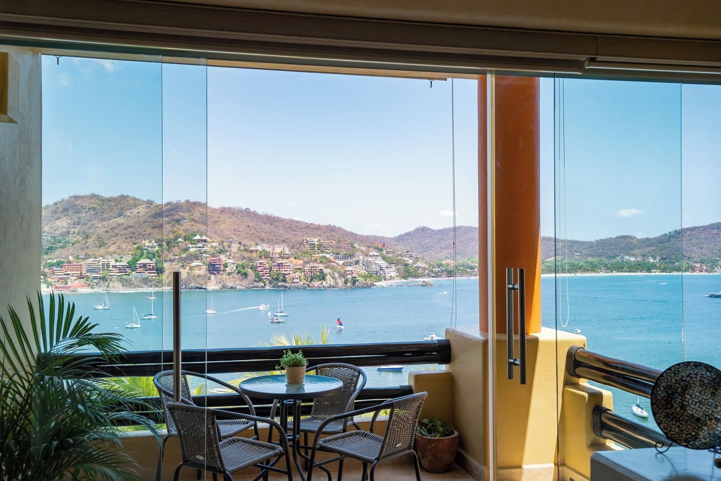 A balcony with a table and chairs, overlooking a coastal town and body of water.