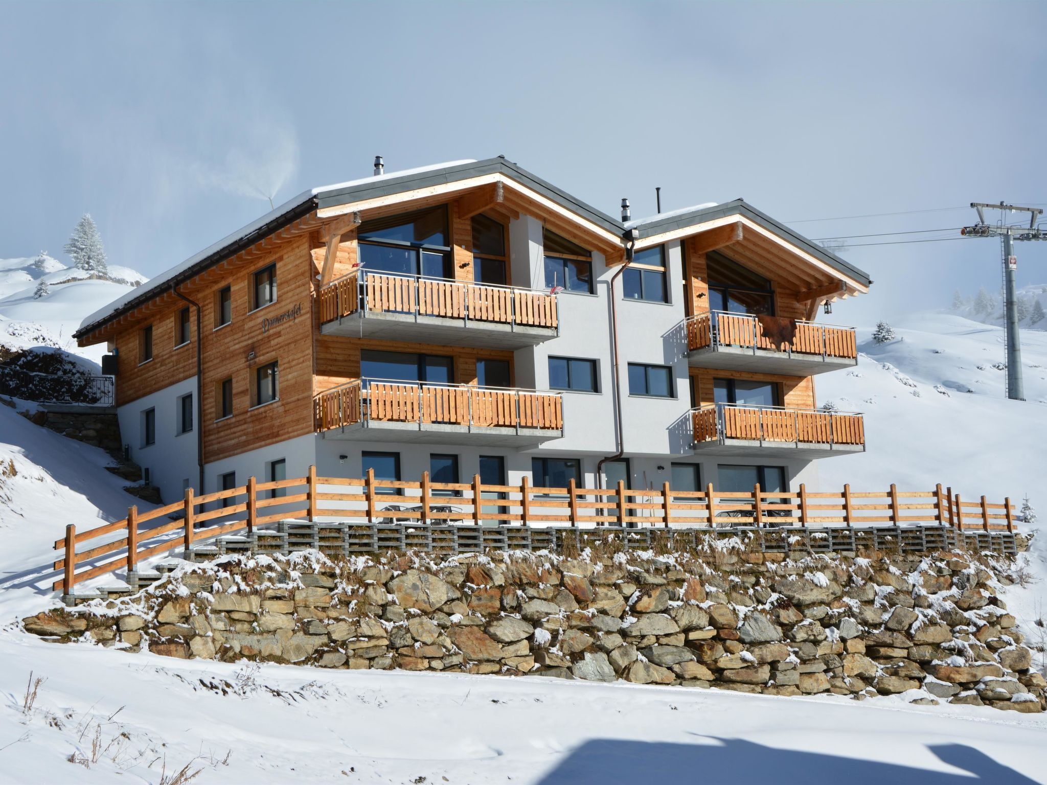 Een meerlaags gebouw met houten balkon, gelegen tegen een besneeuwde berg.
