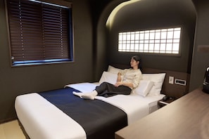 A single bed with a headboard, a bedside table, a window with blinds, and a wall-mounted light fixture. - Cave Ryokan Hotel by Anook Gangbuk Suyu (Seoul)
