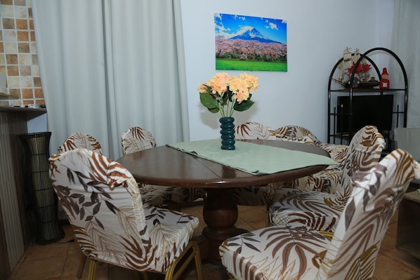 Un comedor con una mesa redonda, sillas estampadas, un jarrón con flores y un cuadro colgado en la pared.