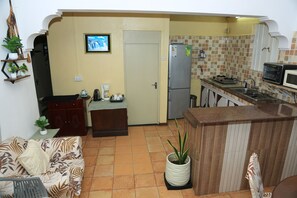 Un espacio habitable compacto con kitchenette, un sofá, una estación de café y una planta en maceta.