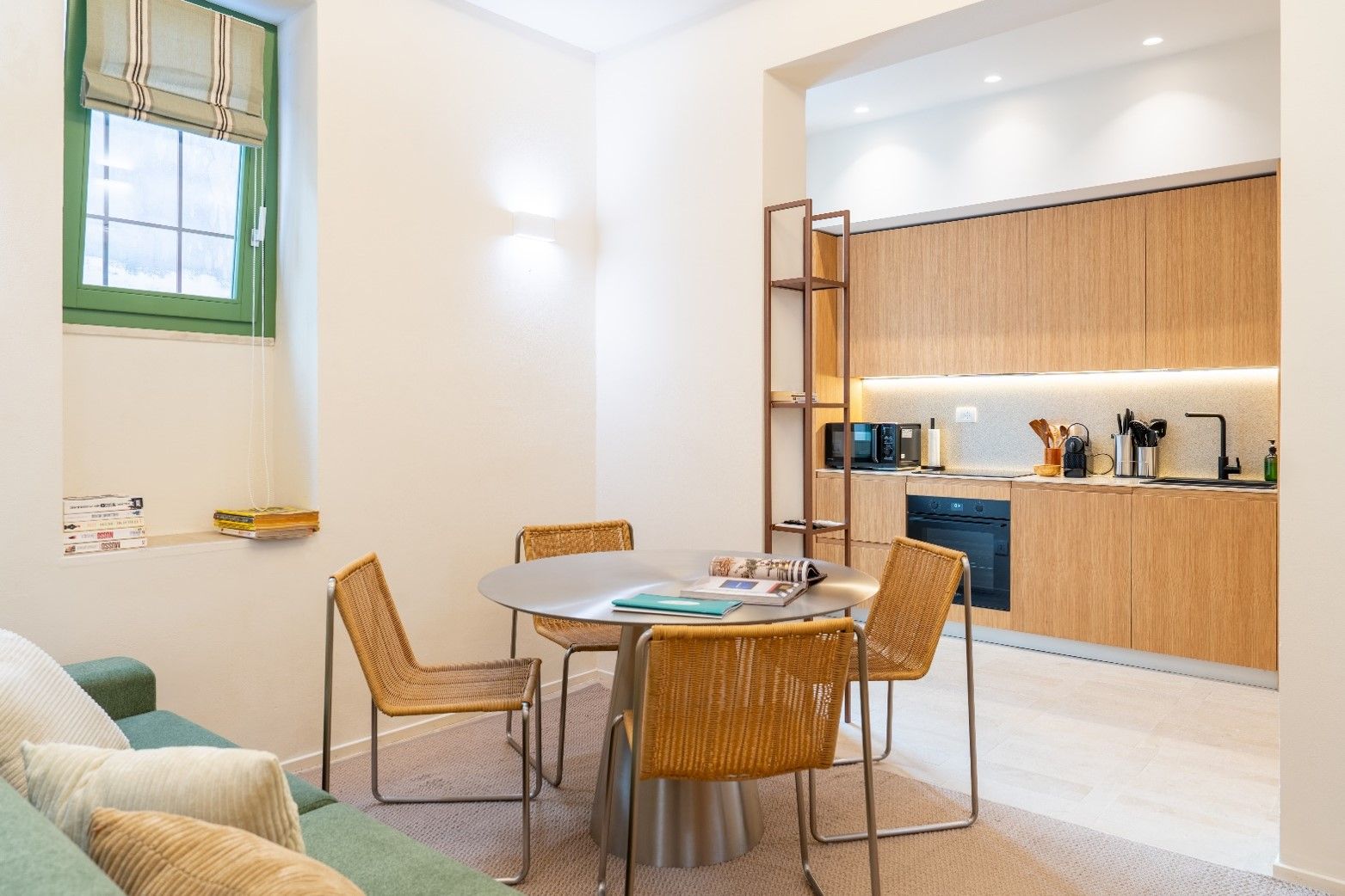 A modern interior with a dining area, kitchen, and a green-framed window.