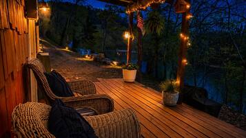 A wooden deck with wicker furniture and potted plants, overlooking a natural landscape at dusk.