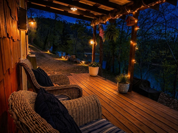 A wooden deck with wicker furniture and potted plants, overlooking a natural landscape at dusk.