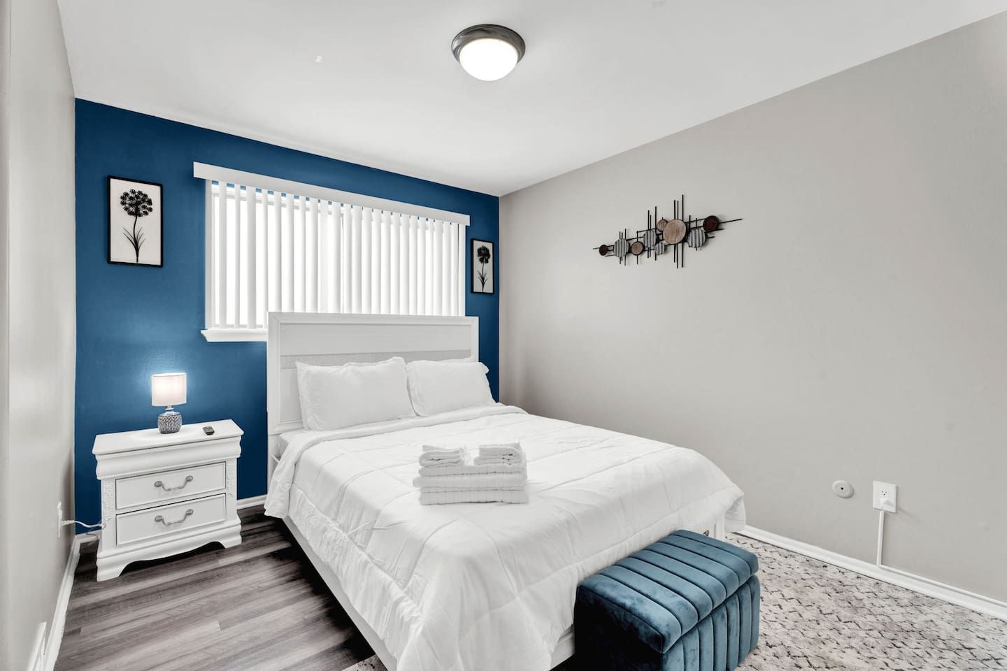 A bedroom with a bed, bedside table, lamp, and a wall decoration.