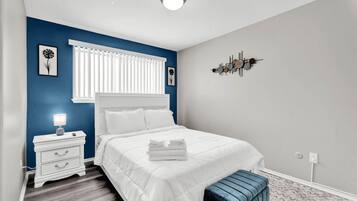 A bedroom with a bed, bedside table, lamp, and a wall decoration.