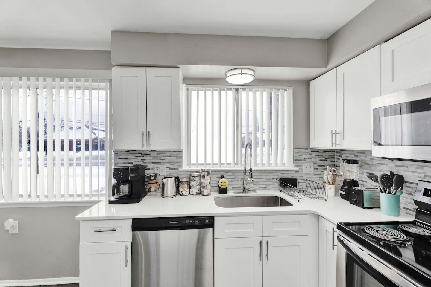 A modern kitchen with white cabinets, a stainless steel refrigerator, a dishwasher, a microwave, and a stove.