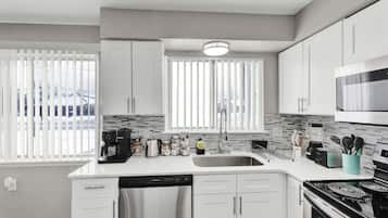 A modern kitchen with white cabinets, a stainless steel refrigerator, a dishwasher, a microwave, and a stove.