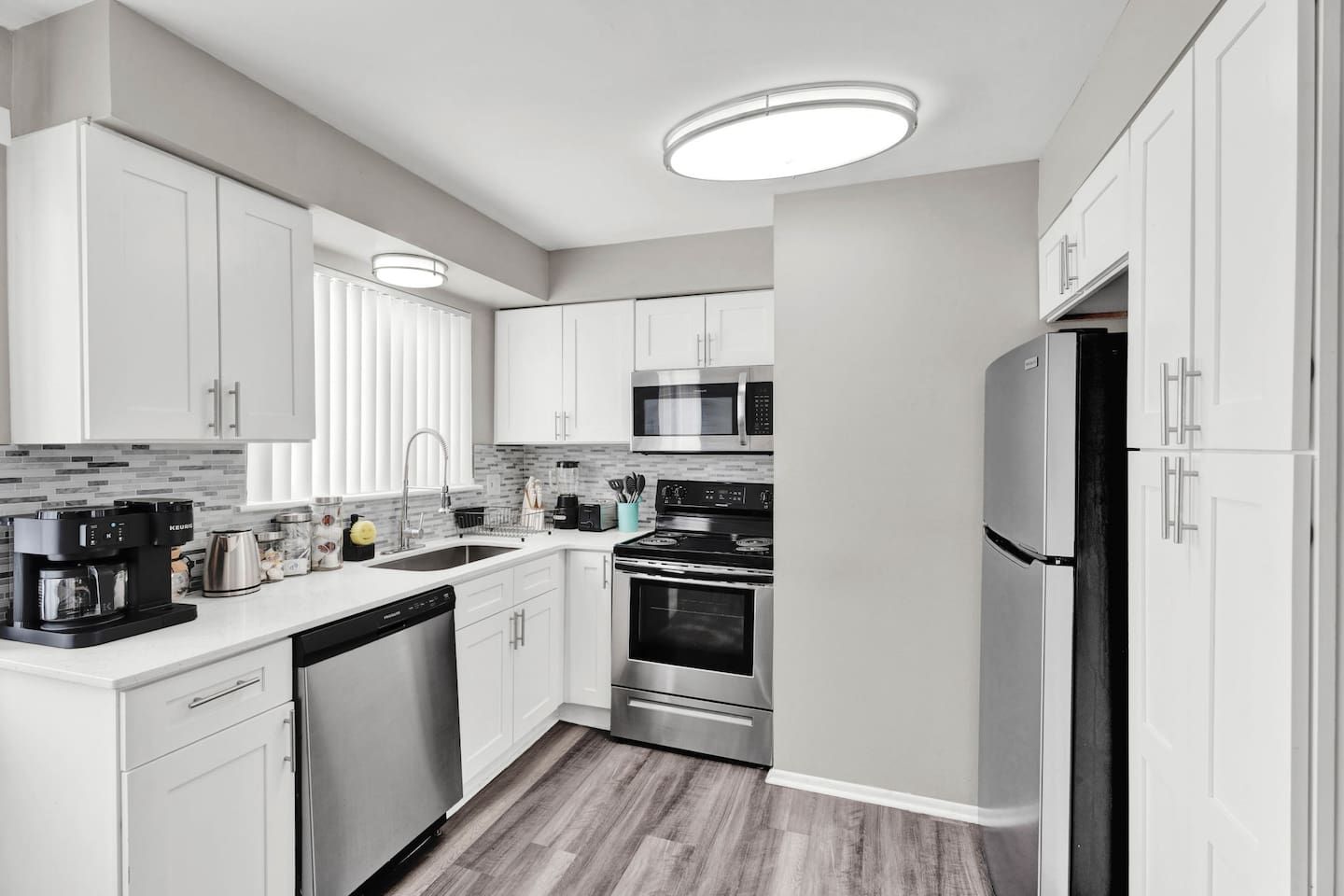 A modern kitchen with white cabinets, stainless steel appliances, and a wooden floor.