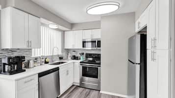 A modern kitchen with white cabinets, stainless steel appliances, and a wooden floor.