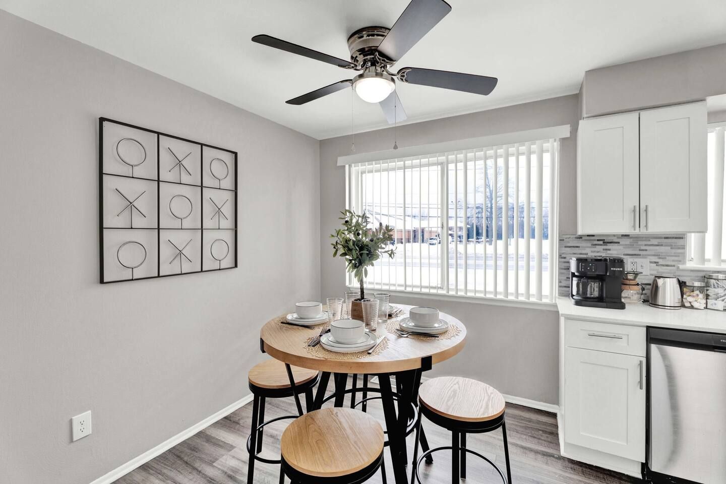 A modern kitchen with a dining area, white cabinetry, a ceiling fan, and a window with blinds.