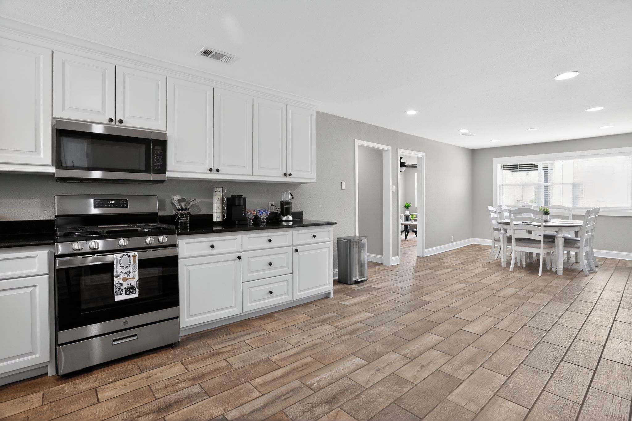 Une cuisine moderne avec des armoires blanches, des appareils en acier inoxydable et un parquet en bois disposé en chevrons.