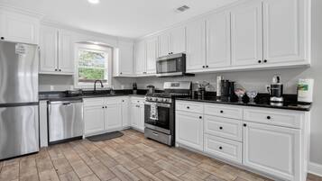 Una cocina moderna con armarios blancos, electrodomésticos de acero inoxidable y un suelo de madera en espiga.