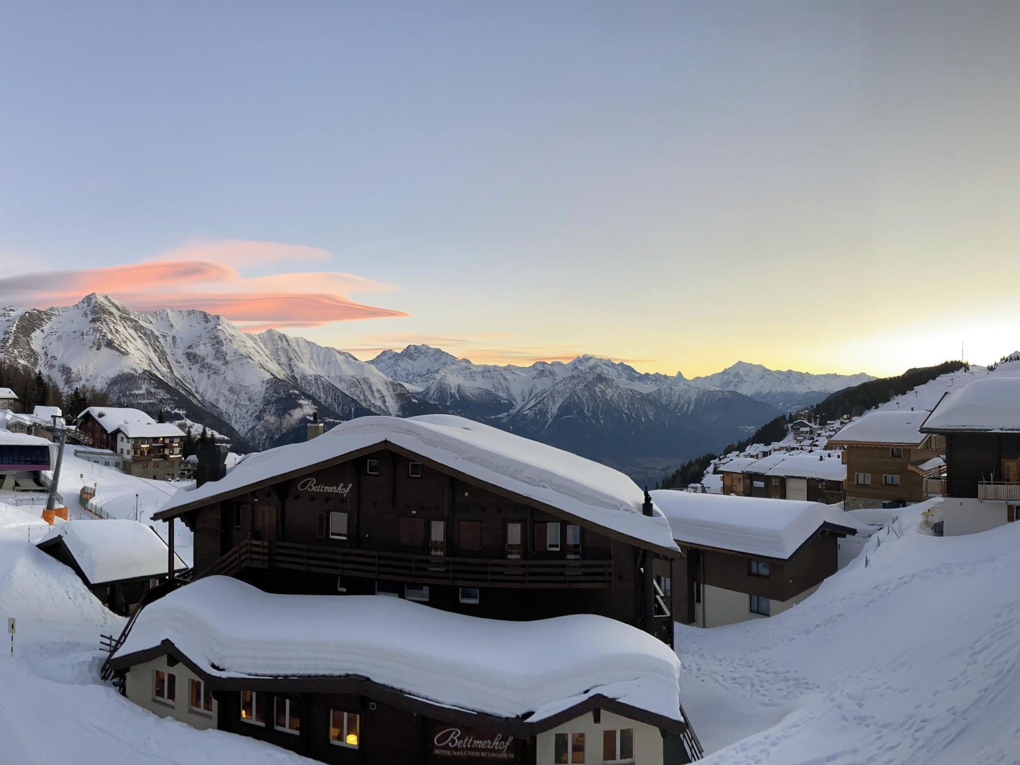 Un pueblo cubierto de nieve en la montaña con edificios tradicionales de madera, incluyendo un hotel llamado 'Bettmerhof'.