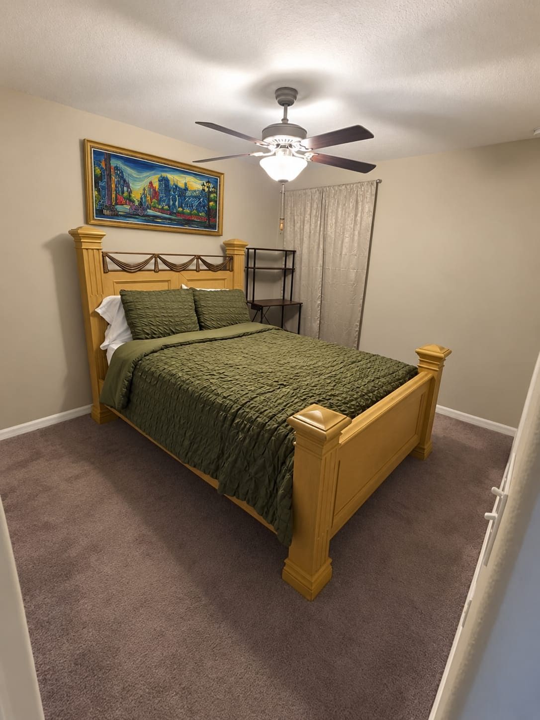 A bedroom with a bed, a ceiling fan, a painting, and a window with curtains.