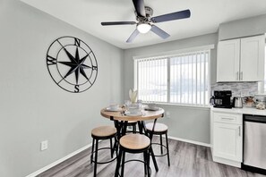 Une cuisine moderne avec un coin repas, dotée d’un ventilateur de plafond, d’une décoration murale représentant une boussole et offrant une vue par la fenêtre.