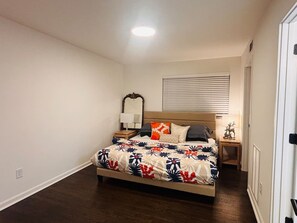 Ein Schlafzimmer mit Bett, Nachttischen, einem Spiegel und einem Fenster mit Jalousien.