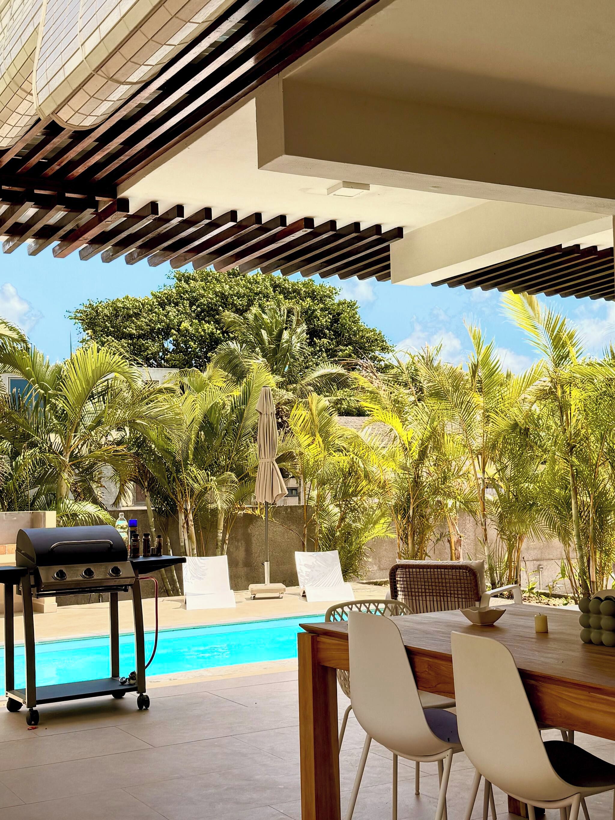 An outdoor pool area with a grill, lounge chairs, and a dining table.