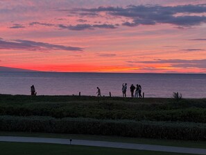 Un atardecer sobre una masa de agua con gente de pie en una zona cubierta de césped.