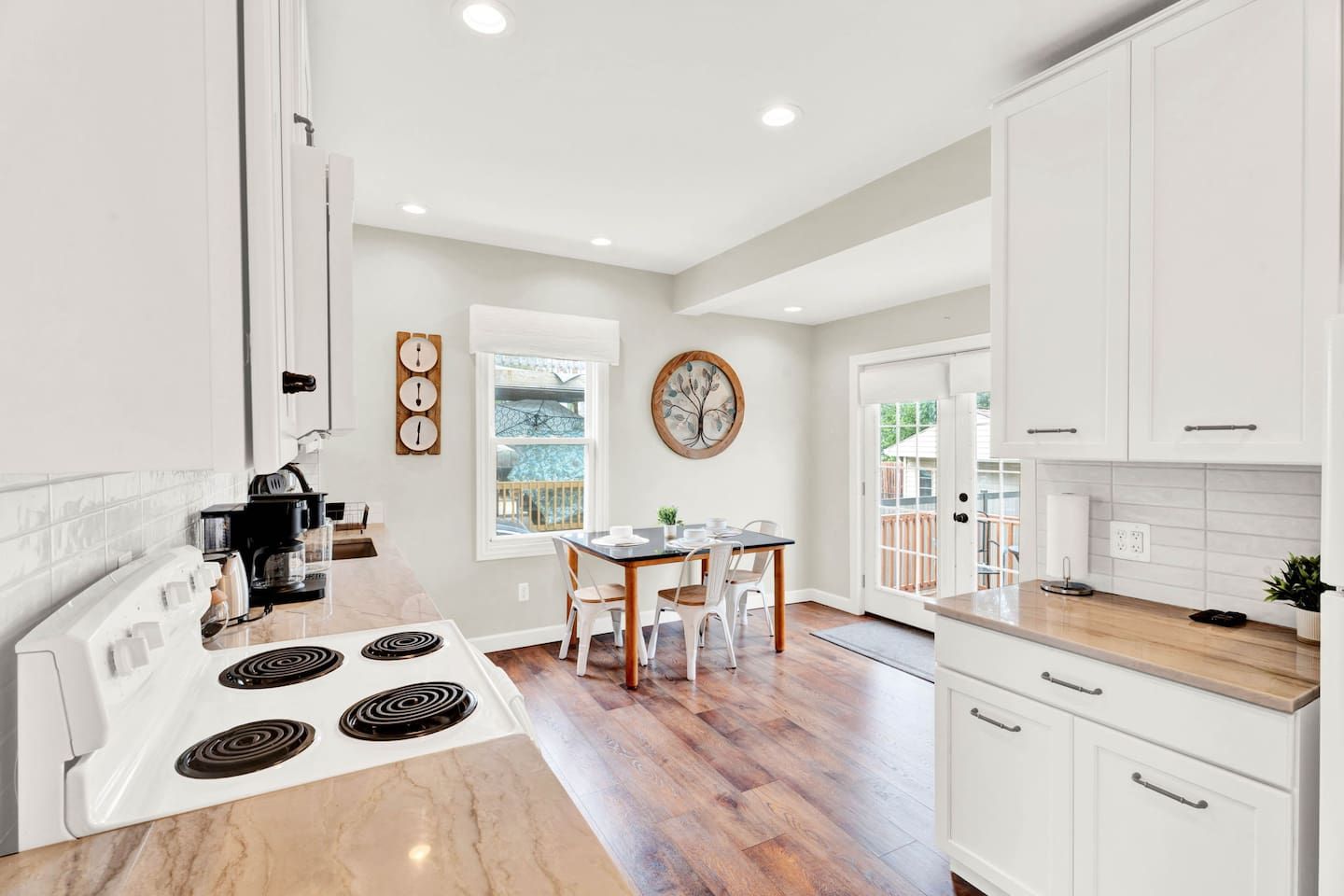 A kitchen with white cabinets, a dining table with chairs, a coffee maker, and a window.