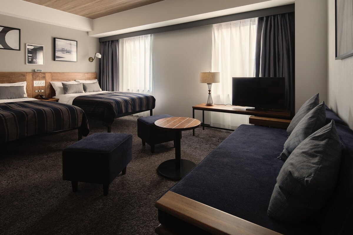 A hotel room with two beds, a sofa, a TV, and a small table.