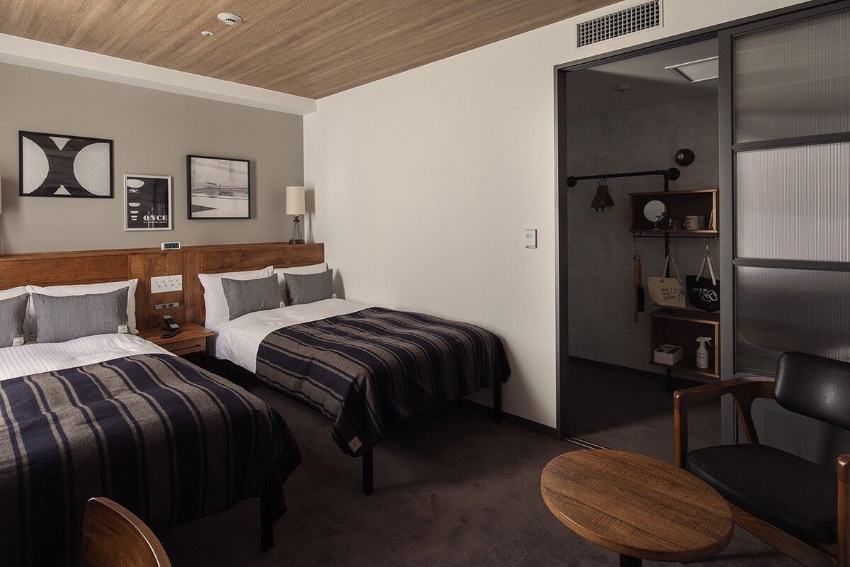 A hotel room with two beds, a desk, a chair, and a wardrobe.