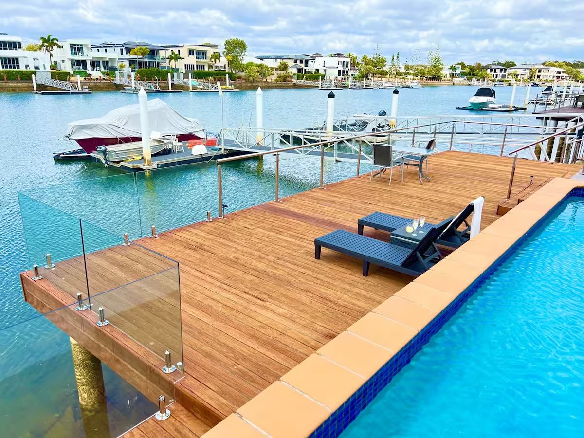 A wooden deck with a pool, lounge chairs, and a view of the marina with boats.