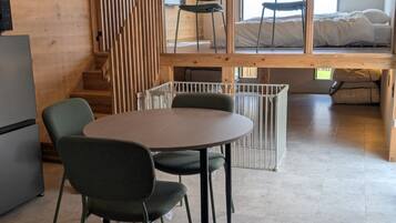 A room with a round table and chairs, a bed, a window, and a staircase.