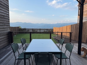 A deck with a table and chairs, a wooden fence, and a view of mountains.