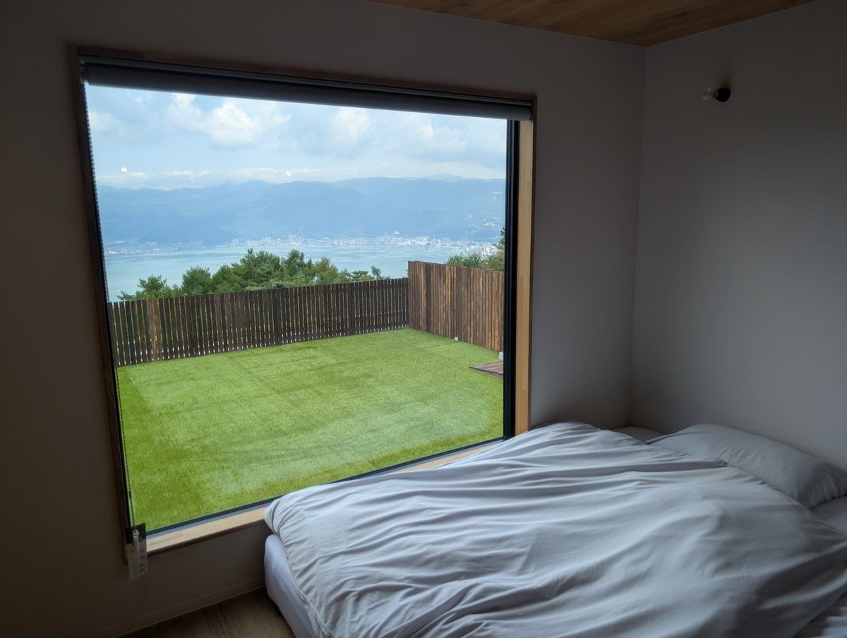 Un dormitorio con un ventanal grande que da a un jardín con césped y vistas al mar.