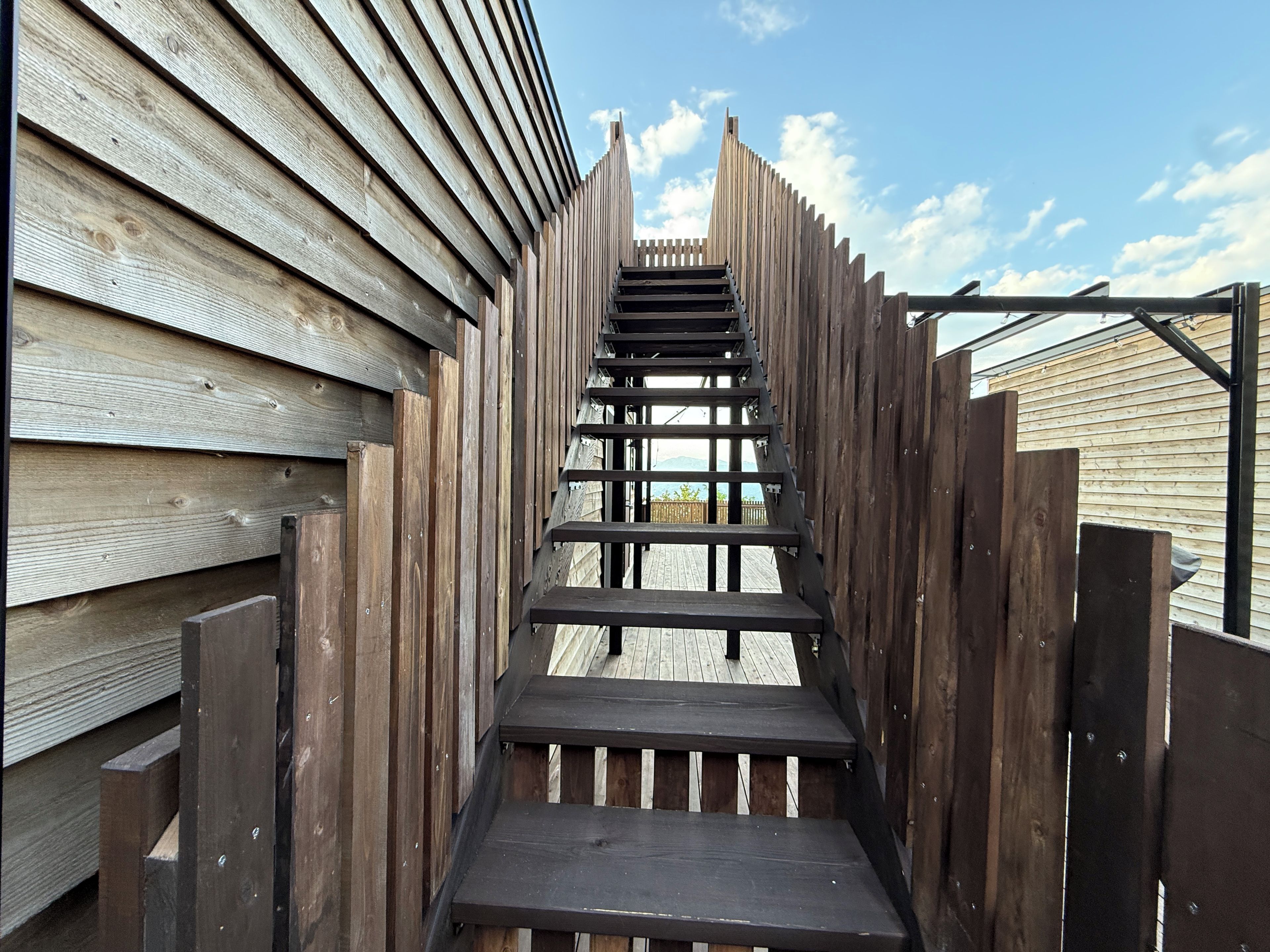 Una escalera de madera que lleva a una terraza con vista a una cerca de madera y un cielo despejado.