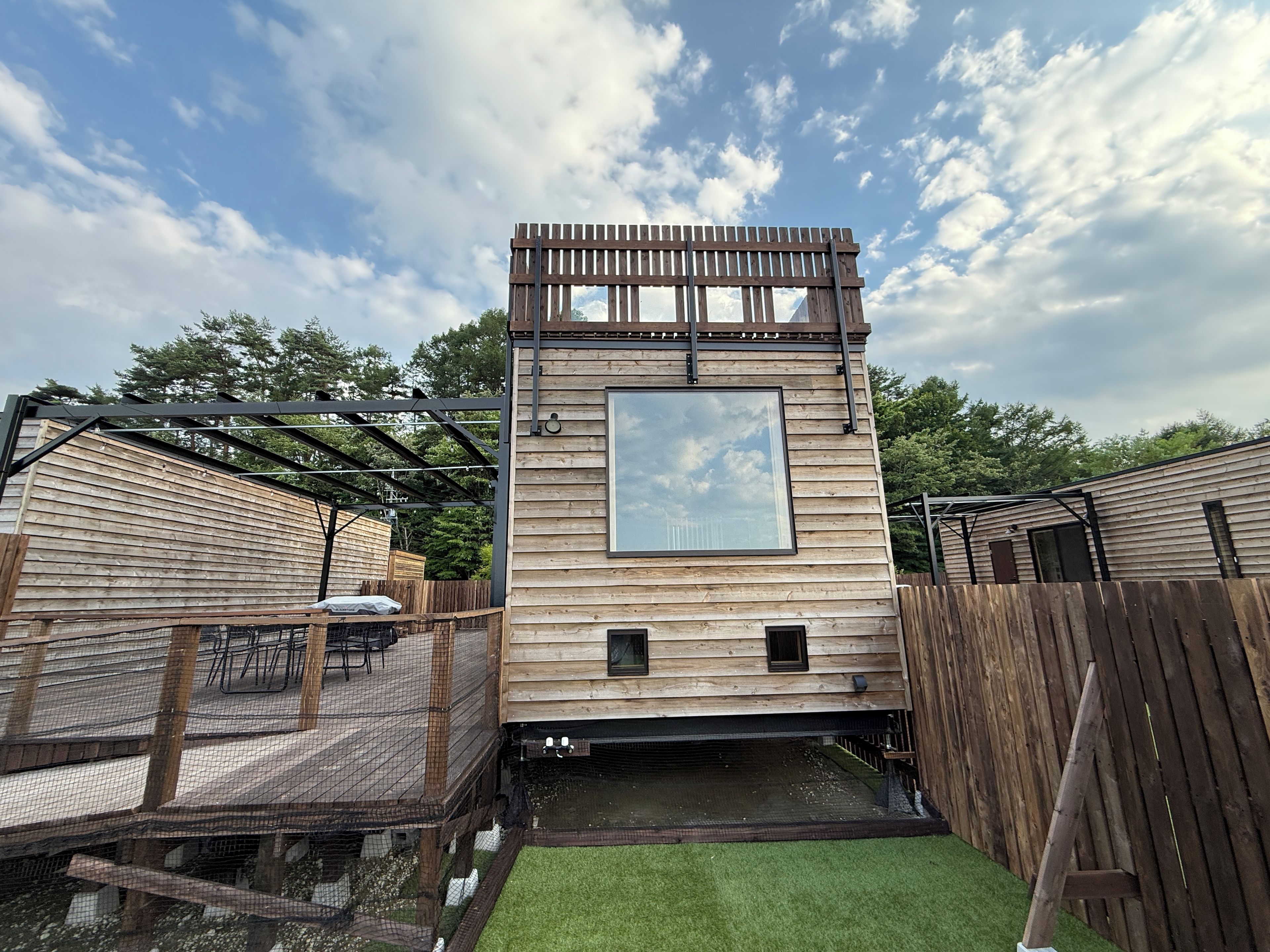 A wooden cabin with a deck, a small pond, and a fenced area.
